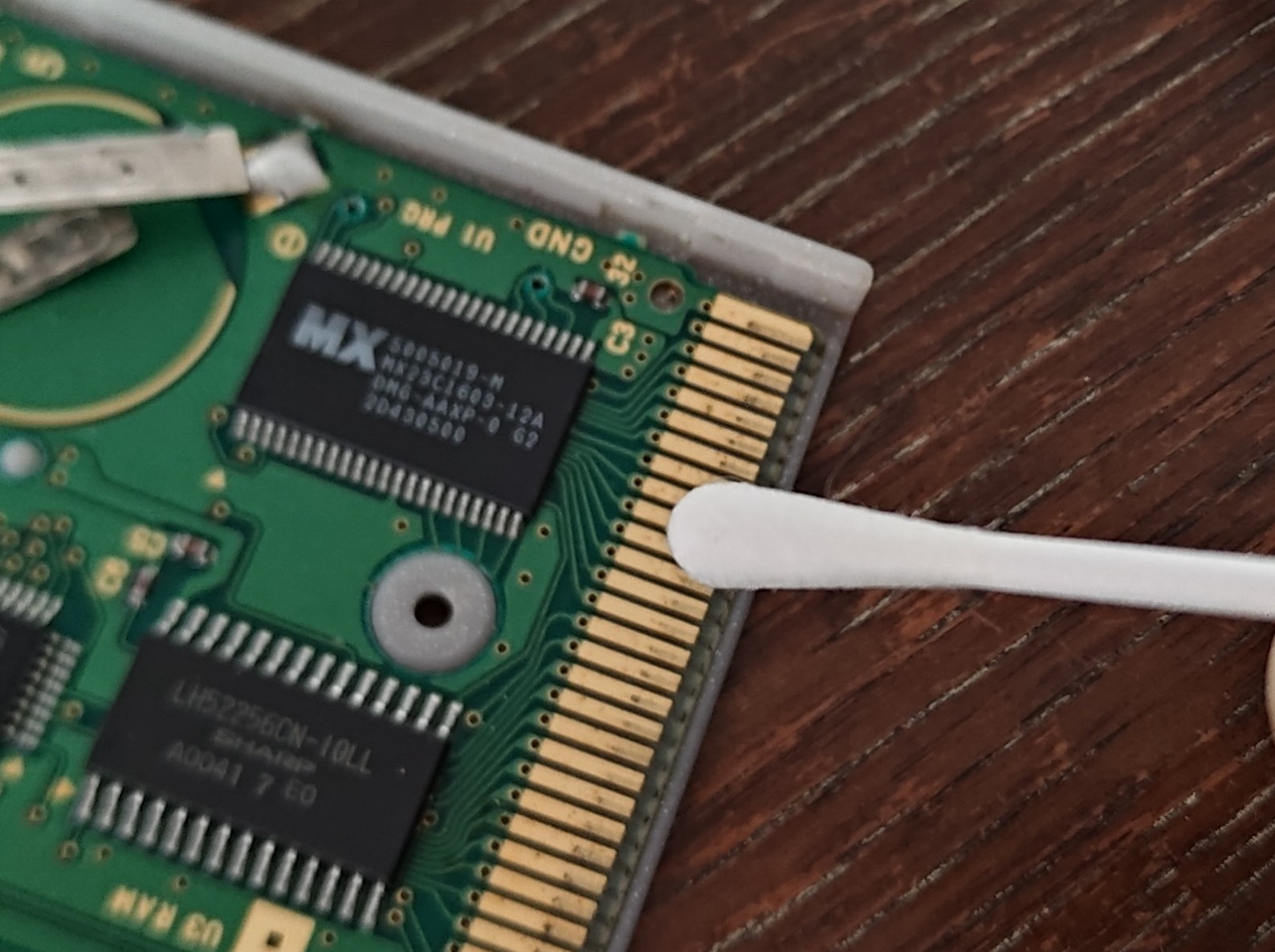 A pure white, damp cotton bud cleaning the tarnished connector on PCB
