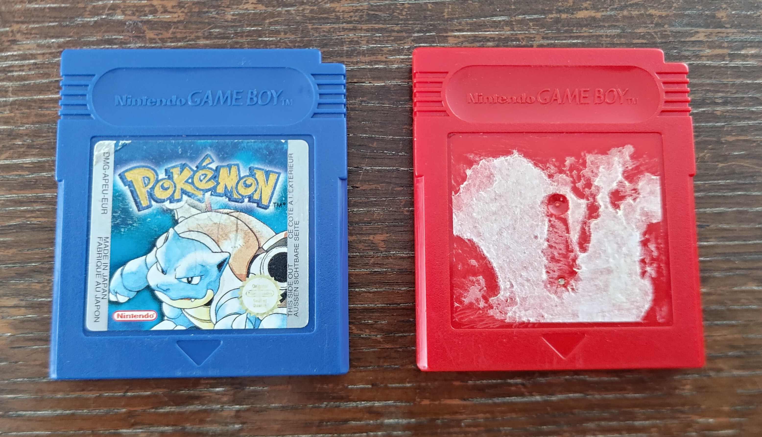 a Pokémon Blue cartridge and a red GameBoy game cartridge with a torn off label