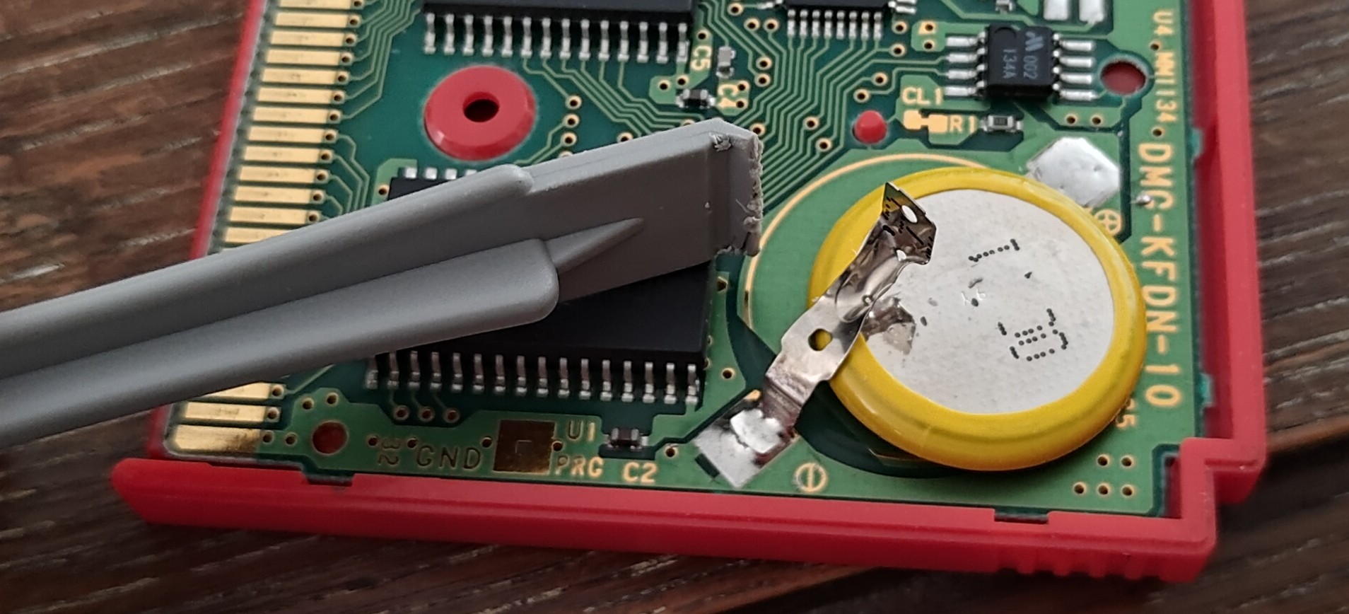 Plastic pry tool with the flat end looking thoroughly chewed up, next to the detached battery and a similarly chewed-looking top tab